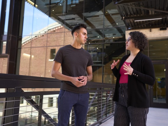Two people having a conversation on the sky bridge connecting Bear Down Gym to Bartlett Academic Success Center 