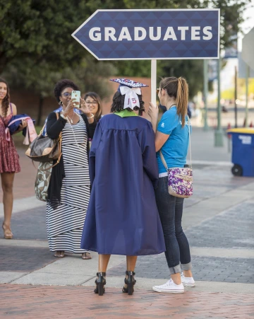A woman wearing U of A cap and gown and standing under a sign that says "graduates"